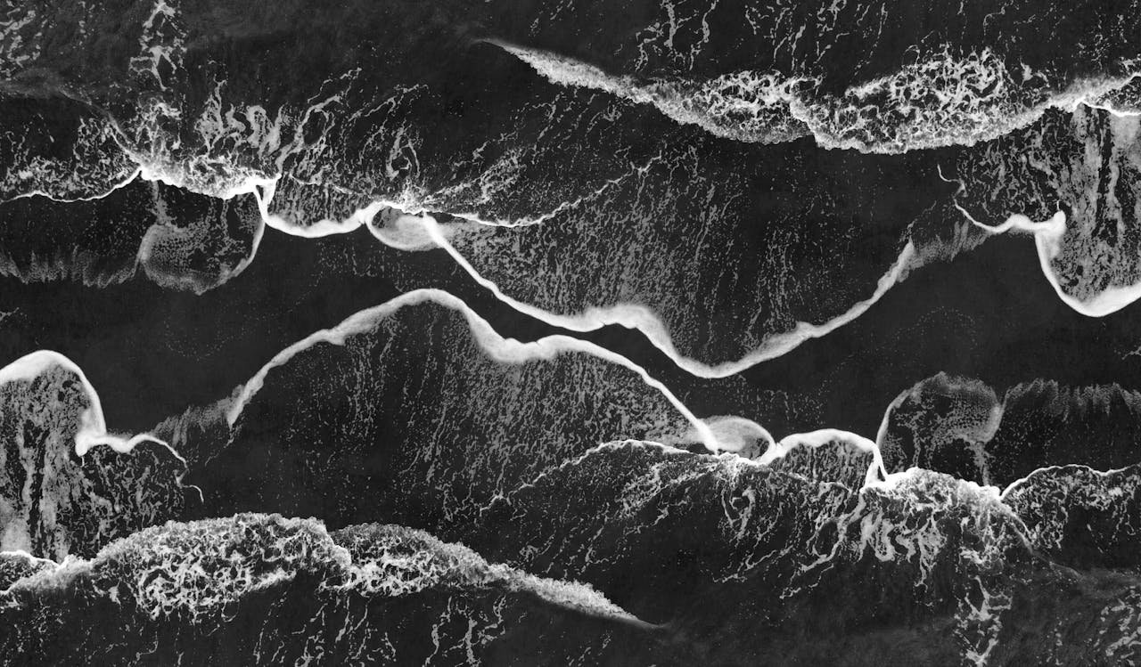 Stunning monochrome aerial shot of ocean waves crashing on the shore, creating abstract patterns.